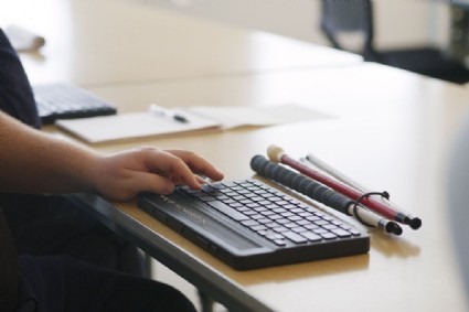 La imagen muestra un teclado qwerty sin la tecla ee y debajo una lnea Braille de 40 caracteres encima de una mesa de madera