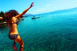 mujer saltando hacia un mar con aguas cristalinas