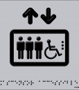 Tres personas de pie y una silla de ruedas metidas en una caja con dos flechas una hacia arriba y otra hacia abajo en color negro con fondo aluminio gris y braille