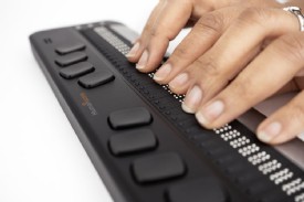 Dispositivo visto de lado con las naos de una personas leyendo Braille