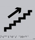 Escaleras con flecha hacia arriba en negro sobre fondo gris, en relieve y braille
