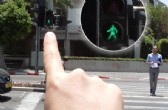 Persona apuntando con el dedo al semáforo de la cera de en frente y el dispositivo le dice de qué color está.
